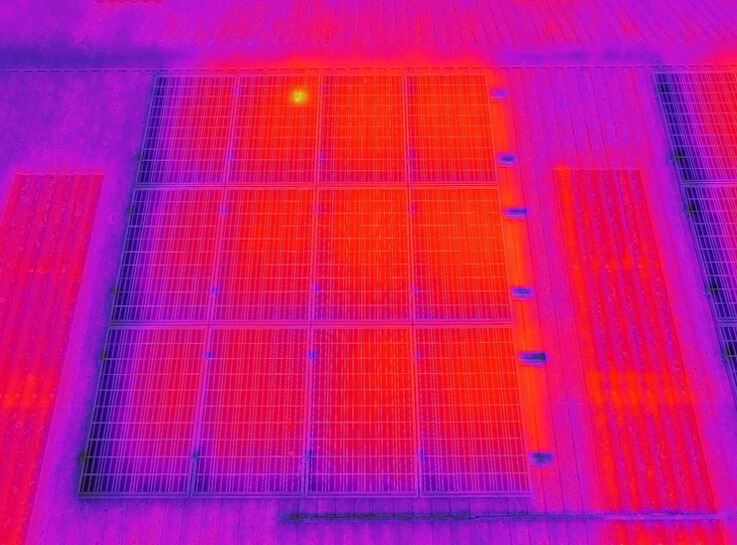 Thermal image of solar panels shows a grid pattern with intense red hues indicating heat. A bright yellow spot stands out in the top area.