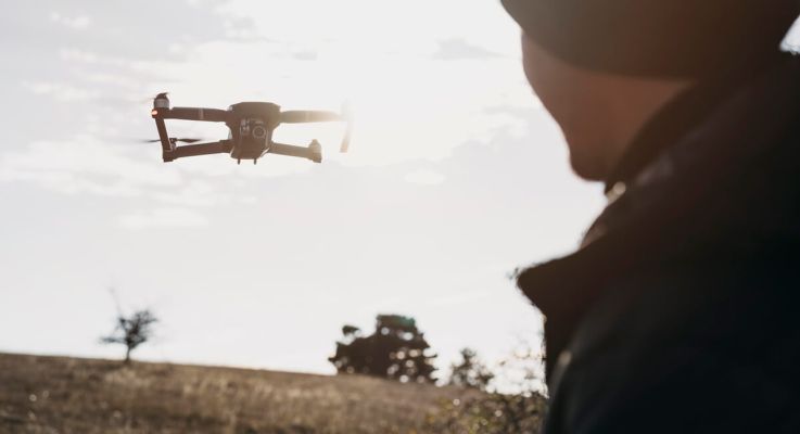 A man operates a drone above a vast green field, showcasing the technology in an outdoor setting.