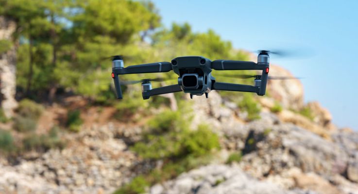 A black drone soaring above a rugged, rocky landscape, capturing aerial views of the terrain below.