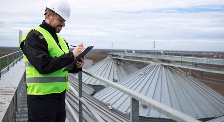 A man wearing a safety vest and hard hat is focused on using a tablet at a construction site.